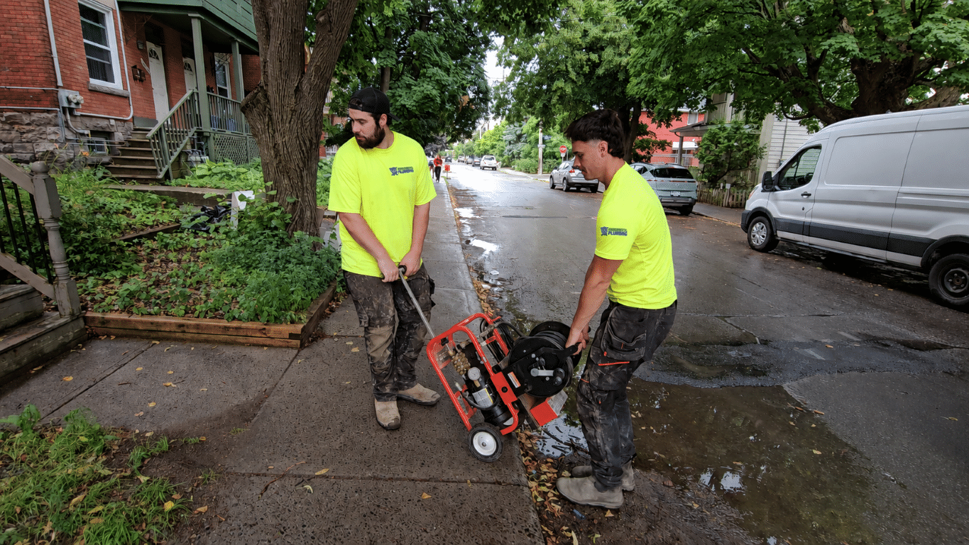 Two Environmental Plumbing technicians handling drain cleaning equipment outdoors